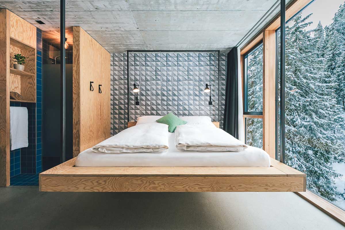 Helles, modernes Hotelzimmer im Riders Hotel Laax mit grossen Fensterflächen und Blick auf den verschneiten Wald – fotografiert von Christian Meixner.