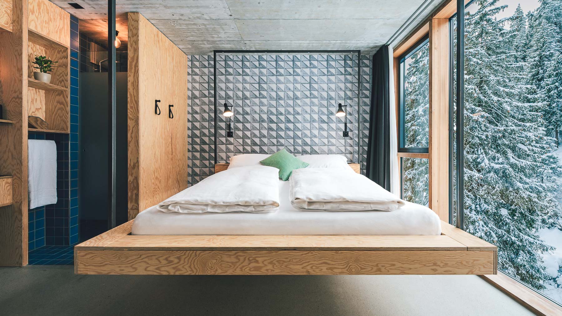 Minimalistisches, lichtdurchflutetes Hotelzimmer im Riders Laax mit Blick auf verschneiten Wald – fotografiert vom Hotelfotograf Christian Meixn