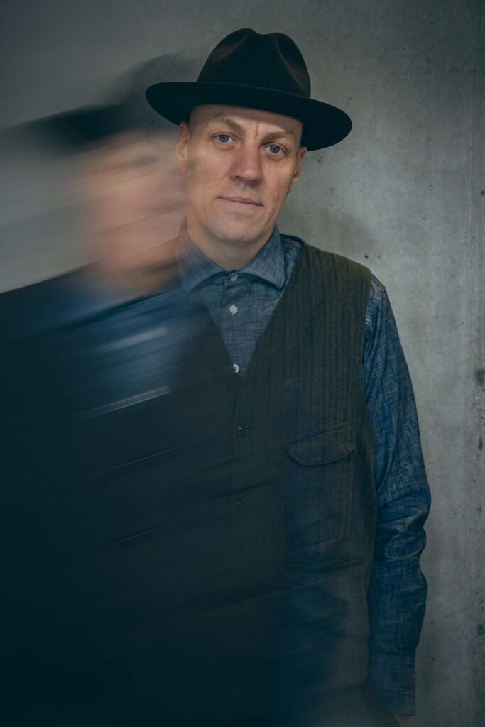 Portraitfotograf Z&uuml;rich: Matija mit Hut vor Betonwand, Portrait mit Bewegungsunsch&auml;rfe